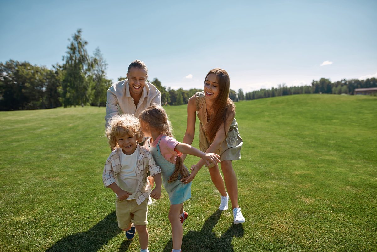 Familie mit zwei Kindern spielt an einem sonnigen Tag auf einer Wiese im Park